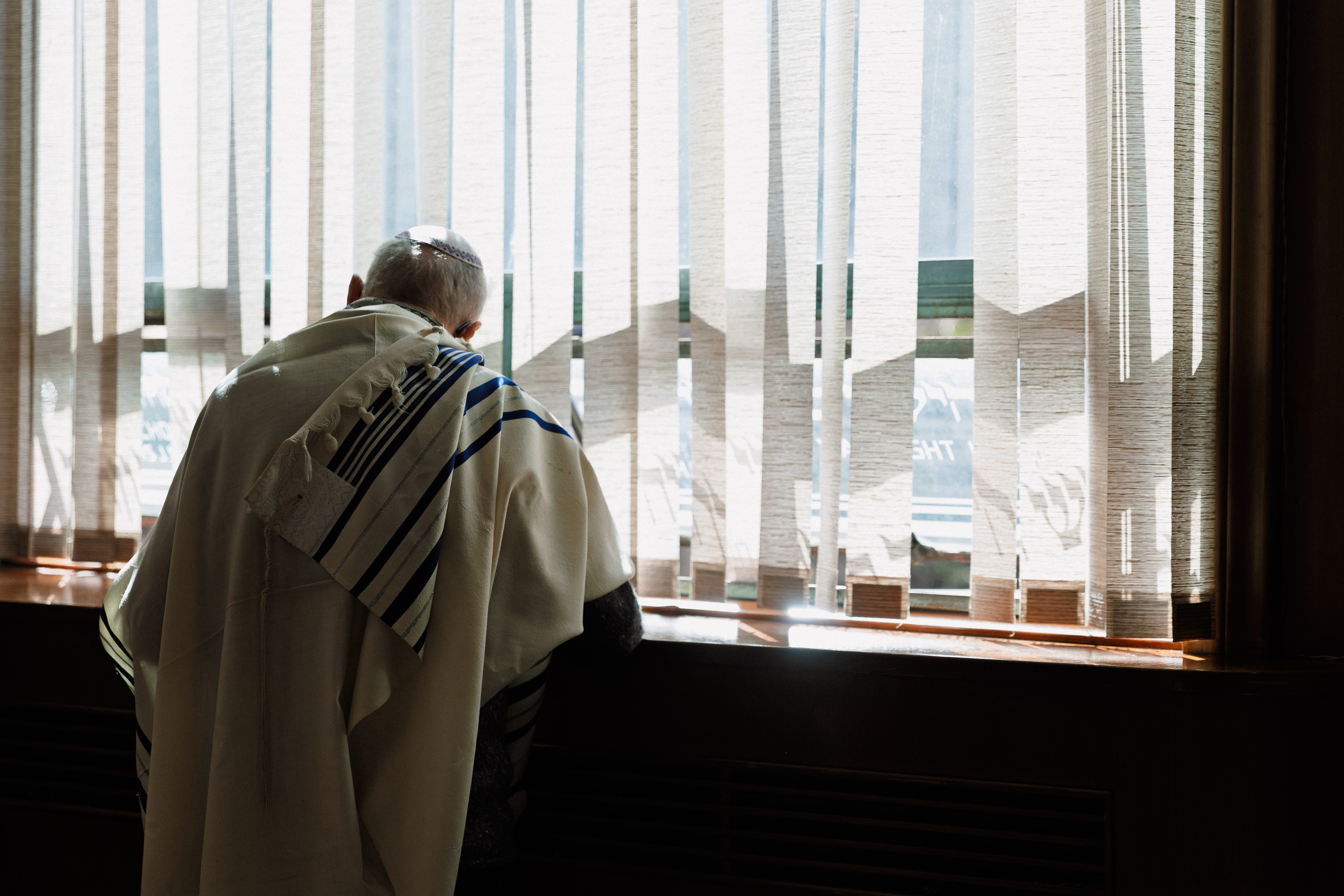 Man wearing a tallit by a window during a Jewish wedding ceremony at a synagogue