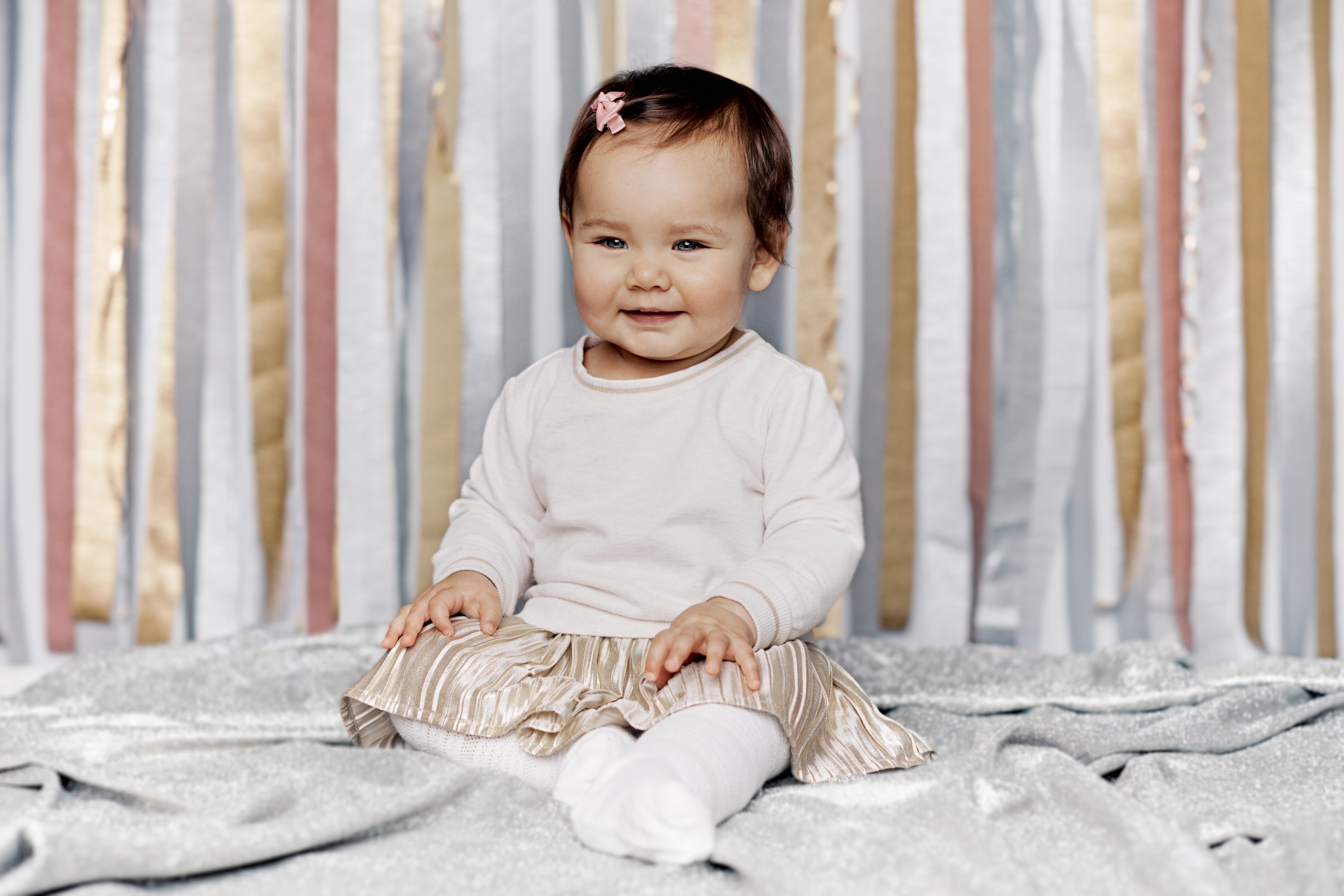 One year old birthday girl sitting in front of streamer background