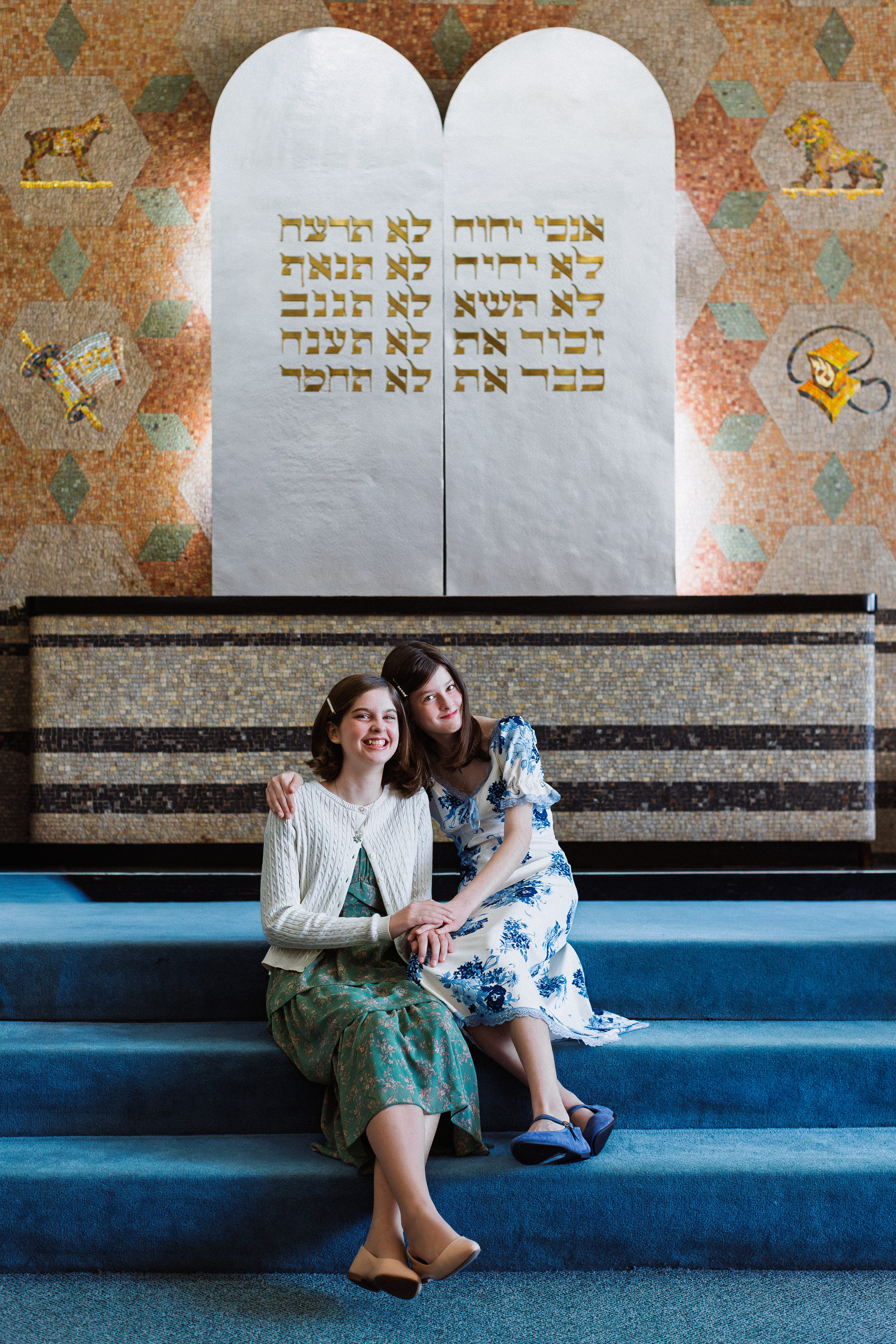 Two young women sitting on the stairs inside a synagogue before a Bat Mitzvah ceremony